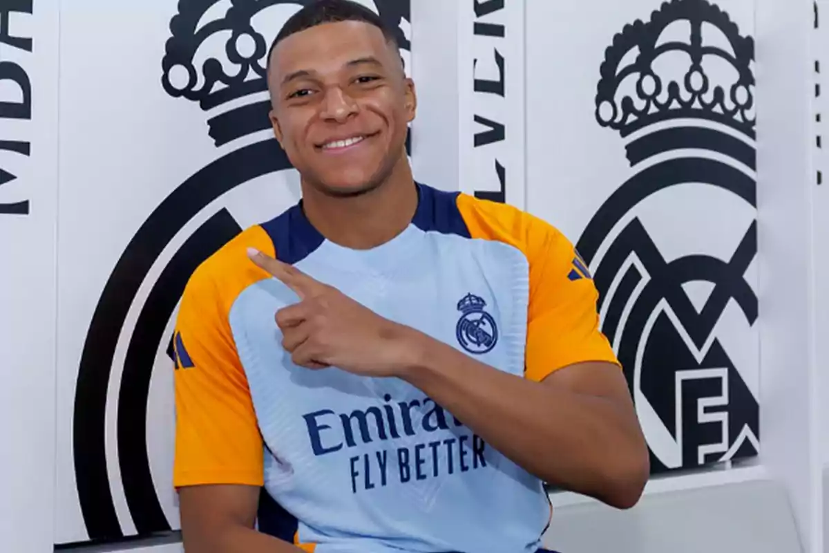 Un jugador de fútbol sonríe y señala con su dedo mientras viste una camiseta de entrenamiento del Real Madrid.