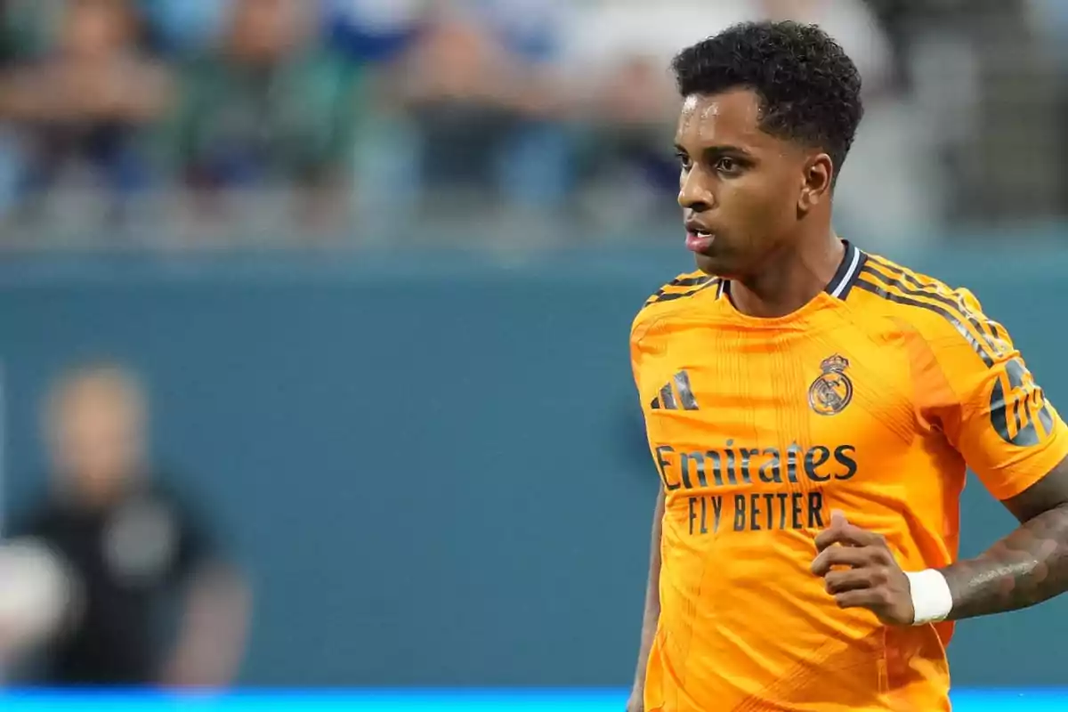 Jugador de fútbol con uniforme naranja del Real Madrid en el campo de juego.