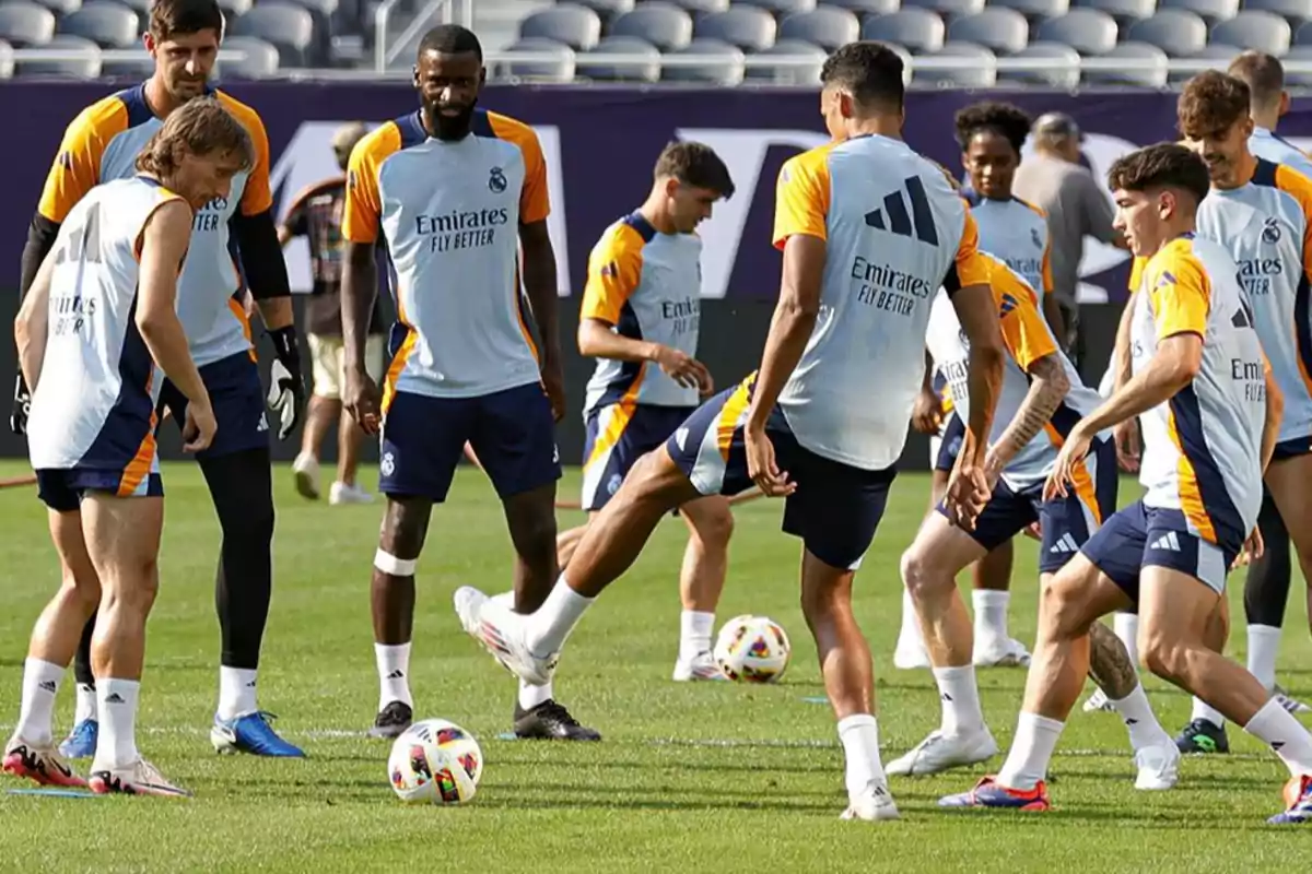 Jugadores de fútbol entrenando en un campo, todos llevan uniformes de entrenamiento con el logo de un patrocinador.