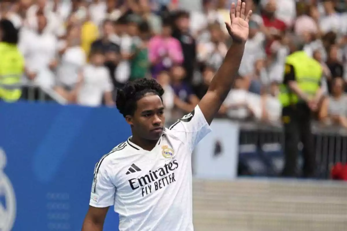 Un jugador de fútbol del Real Madrid levanta la mano en señal de saludo durante un evento deportivo.