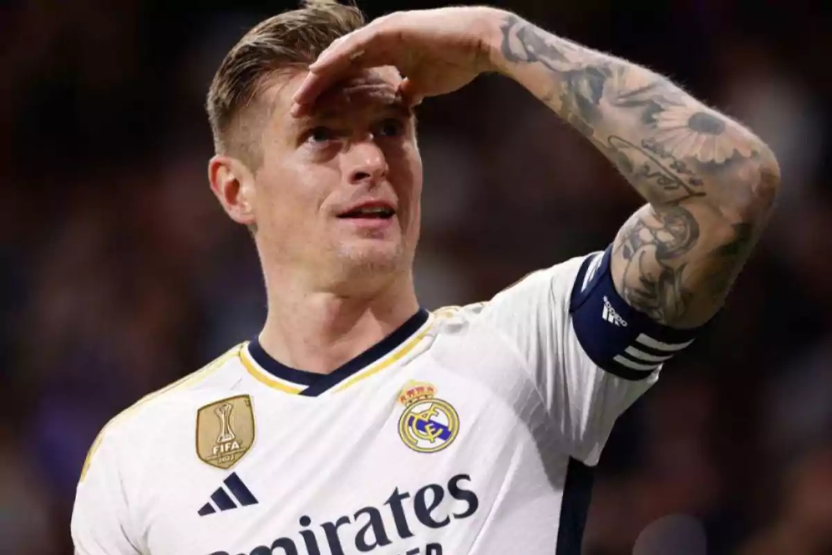 Un jugador de fútbol con el uniforme del Real Madrid, levantando la mano para cubrirse del sol.