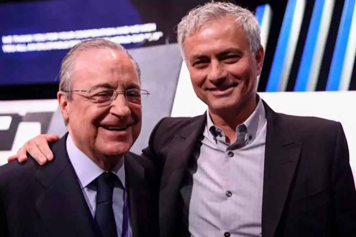 Dos hombres sonrientes posan juntos para una foto, uno de ellos con traje y corbata y el otro con una camisa y chaqueta.