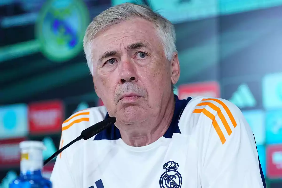 Un hombre con camiseta deportiva blanca y detalles en naranja, hablando en una conferencia de prensa.