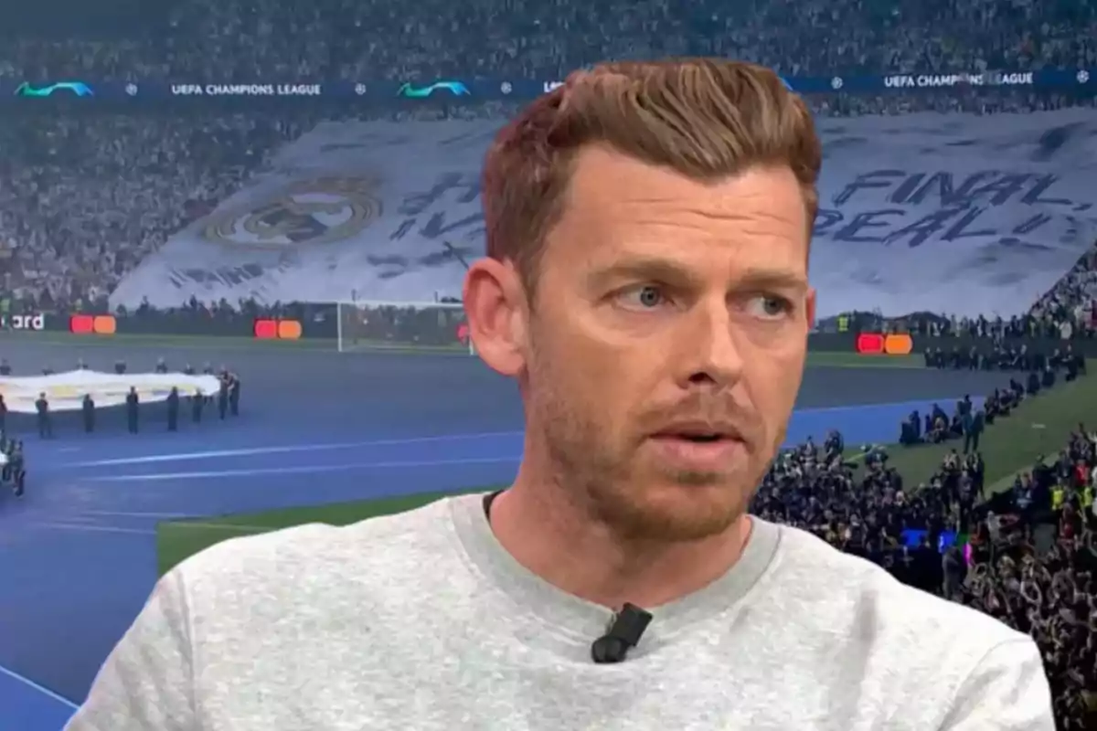 Un hombre hablando frente a una pantalla que muestra un estadio lleno de gente durante un partido de la UEFA Champions League.