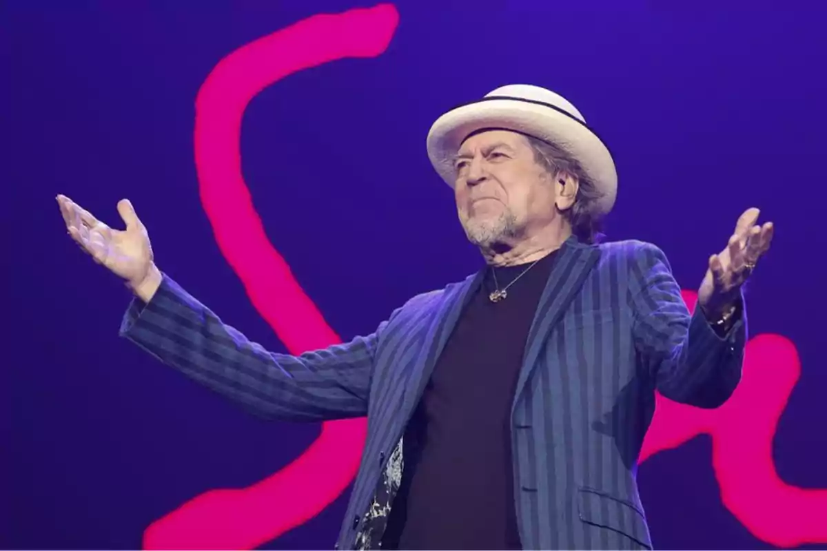 Persona con sombrero y chaqueta a rayas en un escenario con fondo púrpura y rojo. Persona con sombrero y chaqueta a rayas en un escenario con fondo púrpura y rojo.