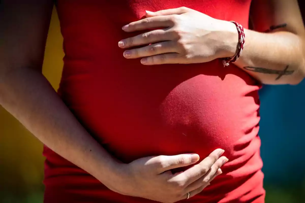 Mujer embarazada con vestido rojo sosteniendo su vientre con ambas manos. Mujer embarazada con vestido rojo sosteniendo su vientre con ambas manos.