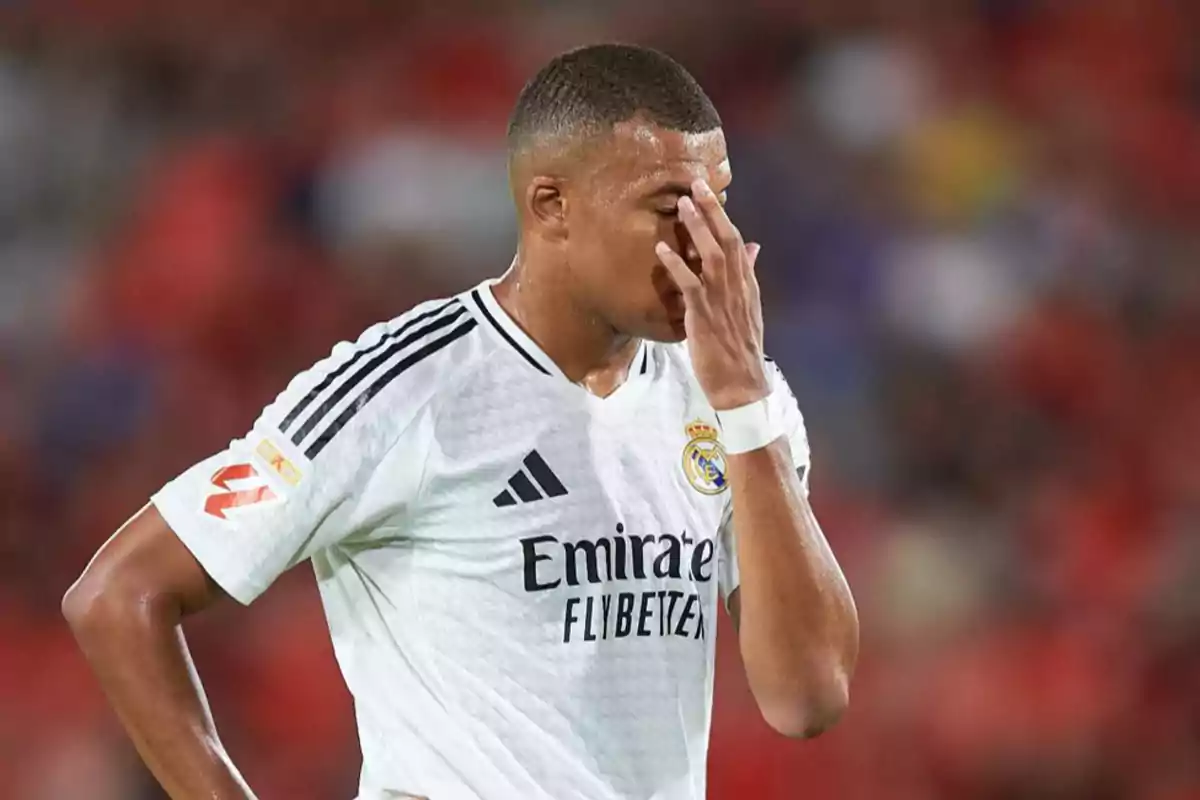 Jugador de fútbol con uniforme blanco del Real Madrid cubriéndose el rostro con la mano en un campo de juego.