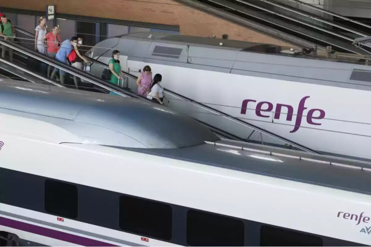 Personas con mascarillas suben por una escalera mecánica junto a trenes de alta velocidad en una estación. Personas con mascarillas suben por una escalera mecánica junto a trenes de alta velocidad en una estación.