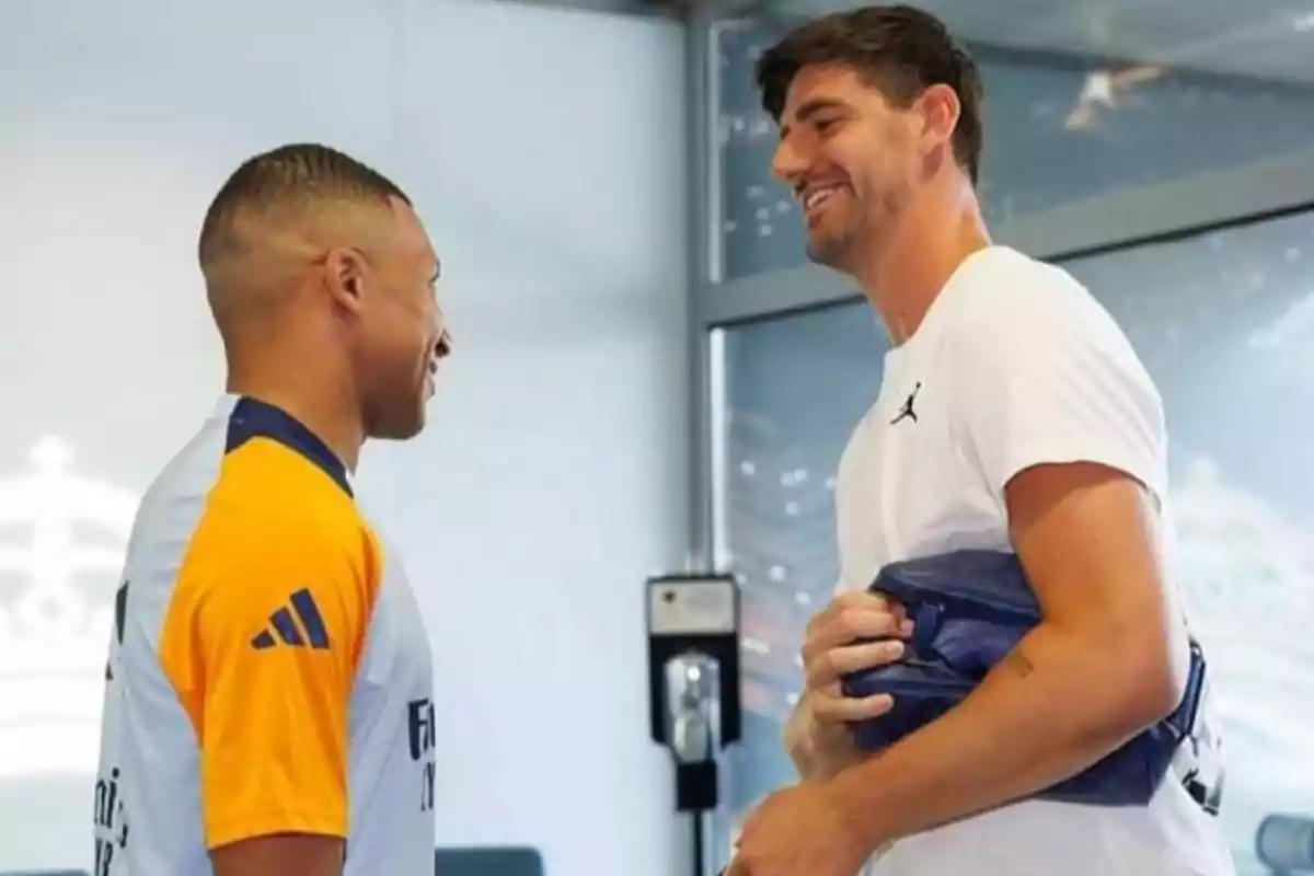 Dos hombres conversando y sonriendo en un entorno deportivo.