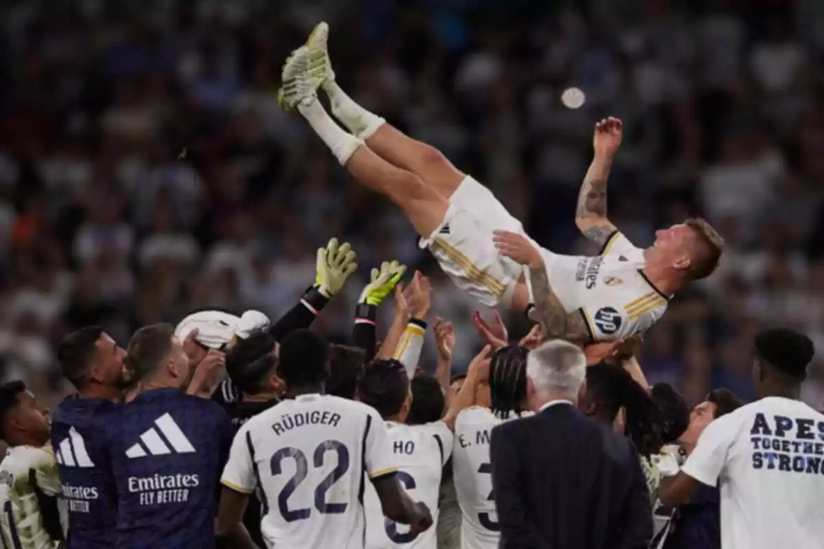 Jugadores de fútbol levantan a un compañero en el aire durante una celebración en el campo.