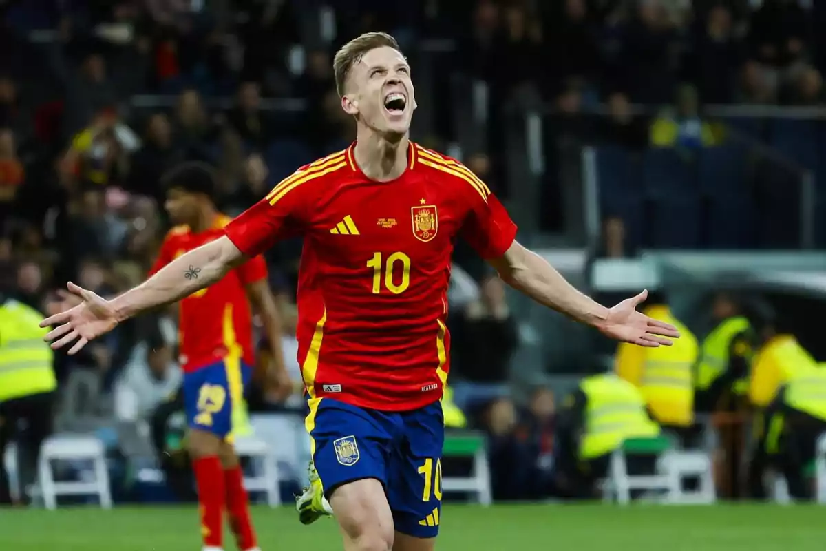 Jugador de fútbol con la camiseta de la selección española celebrando un gol con los brazos extendidos en un estadio.