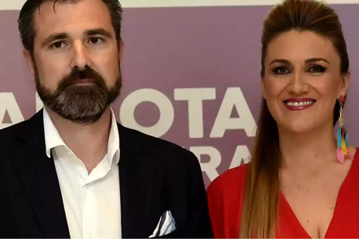 Dos personas posando frente a un fondo morado con letras blancas.