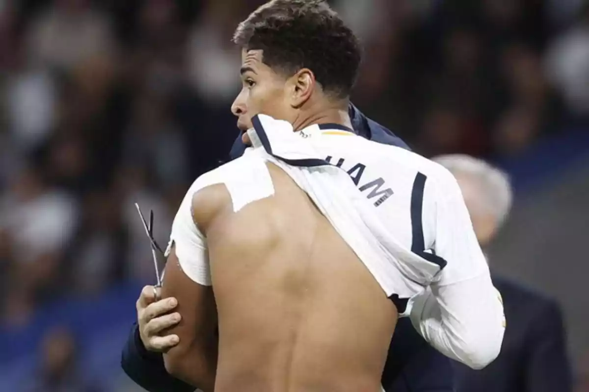 Un jugador de fútbol con la camiseta levantada mostrando su espalda y hombro vendado.