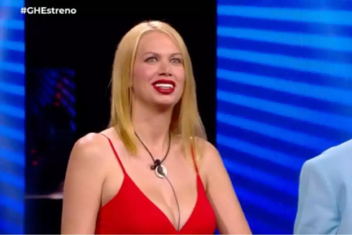 Una mujer con vestido rojo y cabello rubio sonríe en un programa de televisión.