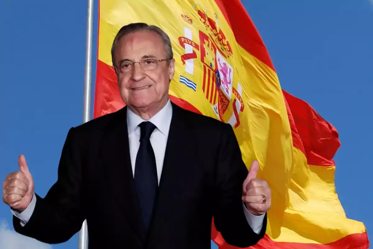 Hombre con traje oscuro y corbata, sonriendo y levantando ambos pulgares, con una bandera de España ondeando en el fondo.