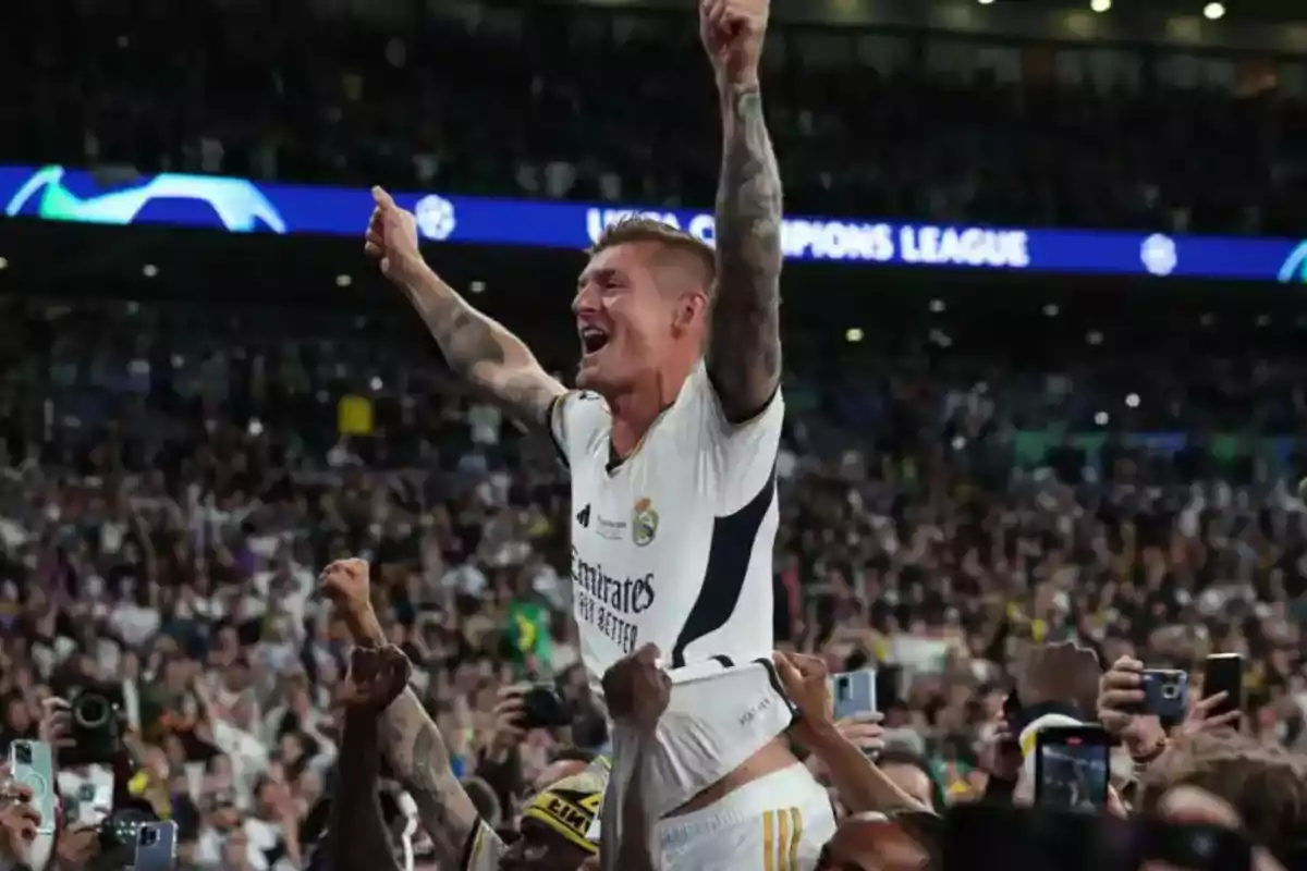 Un jugador de fútbol del Real Madrid es levantado por sus compañeros mientras celebra en un estadio lleno de aficionados.