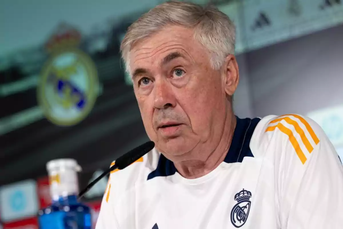 Un hombre con camiseta blanca y detalles amarillos, con el escudo del Real Madrid, hablando en una conferencia de prensa.