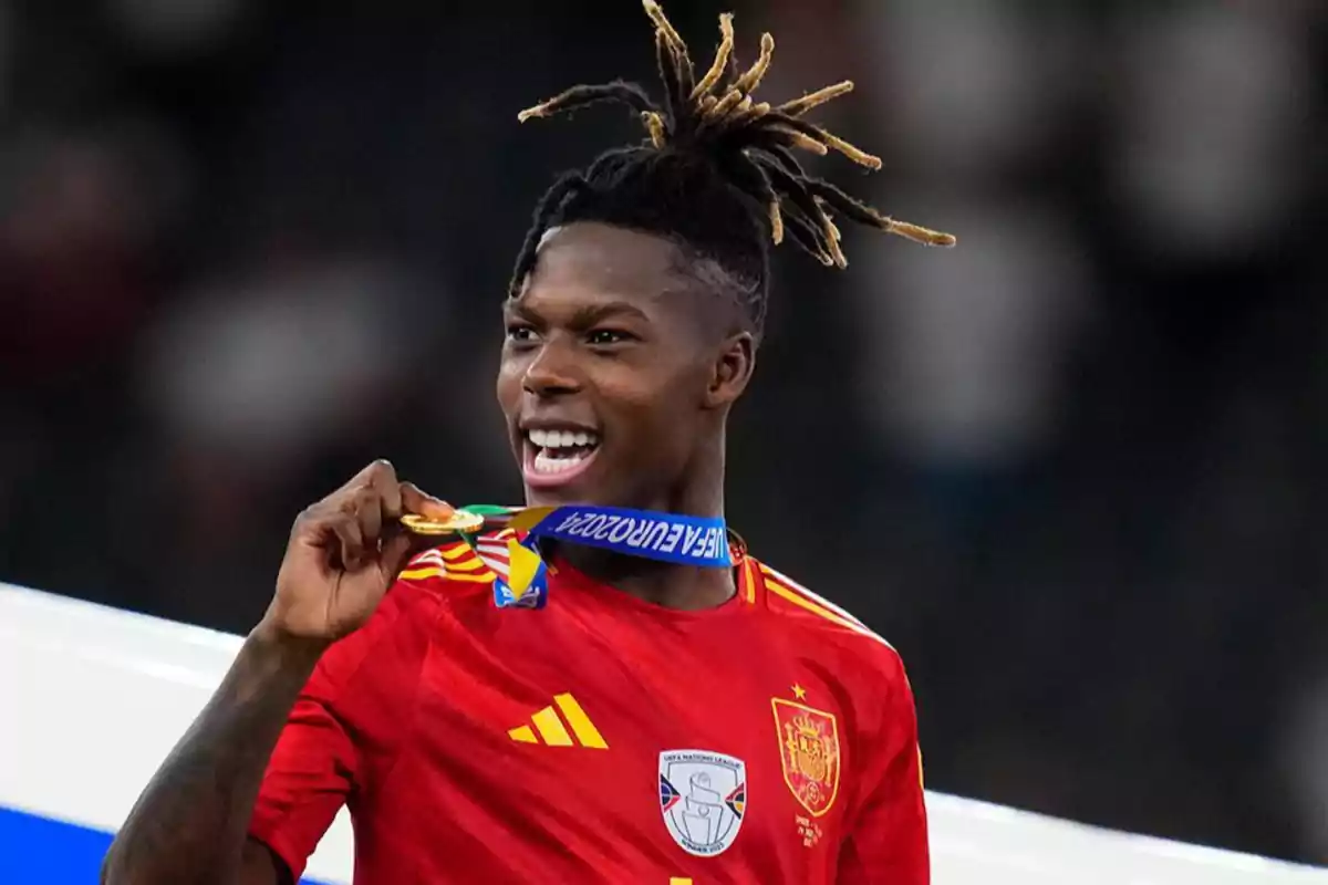 Jugador de fútbol con la camiseta de España mordiendo una medalla de oro.