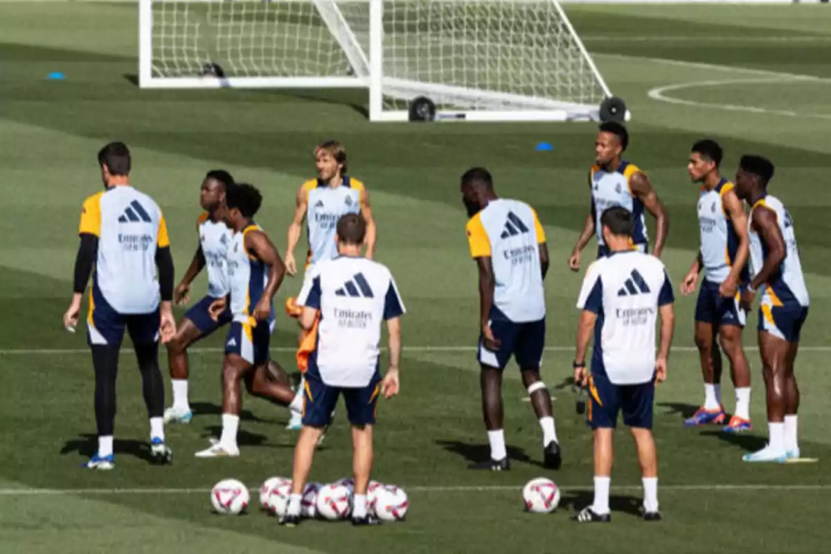 Jugadores de fútbol entrenando en un campo con un entrenador y varios balones.