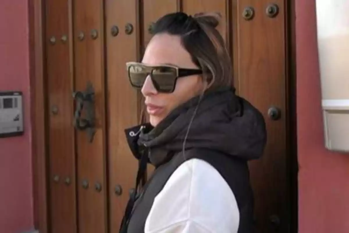 Mujer con gafas de sol y chaqueta oscura frente a una puerta de madera. Mujer con gafas de sol y chaqueta oscura frente a una puerta de madera.