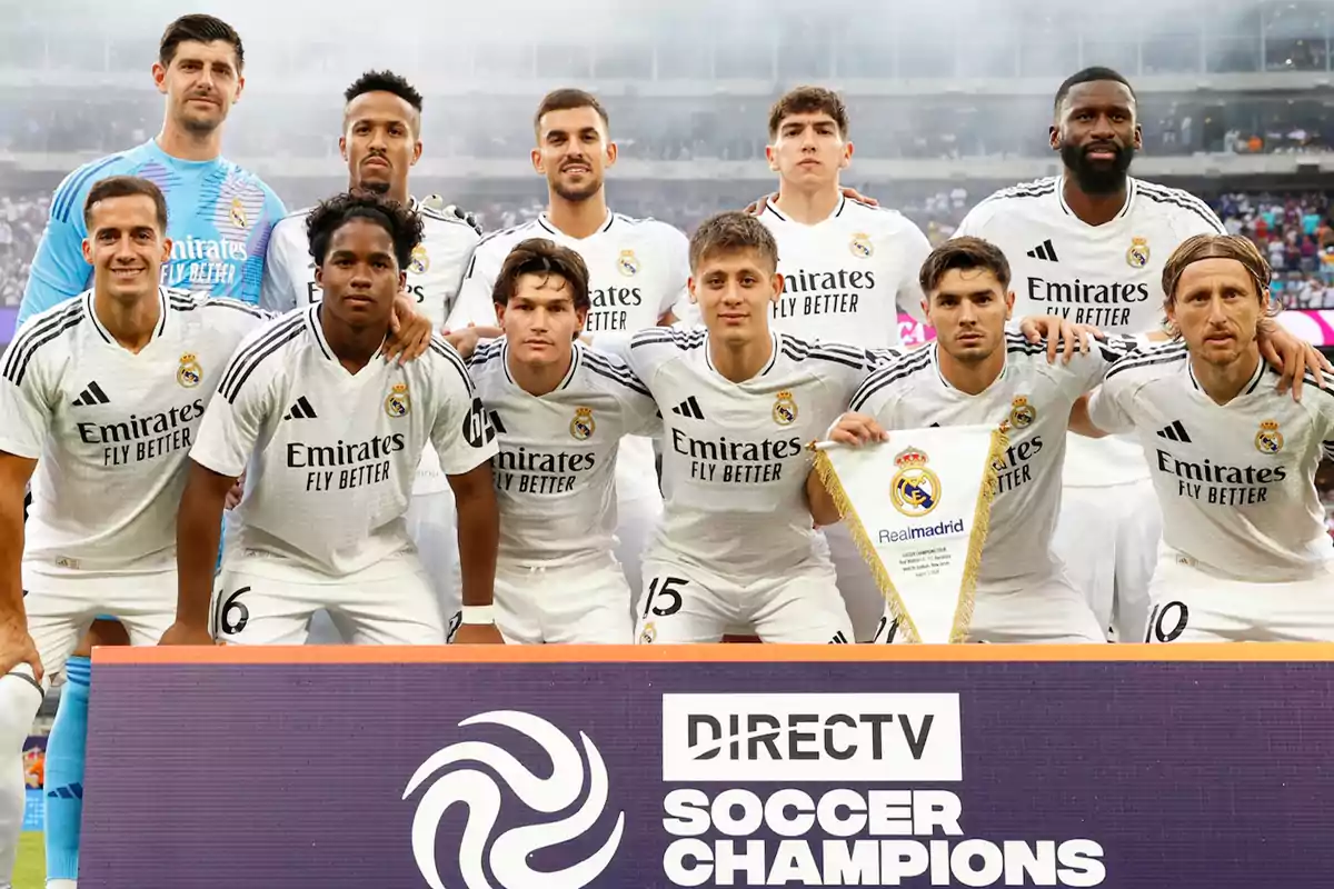 Jugadores del equipo de fútbol Real Madrid posando para una foto grupal antes de un partido, con un cartel de DIRECTV Soccer Champions en primer plano.