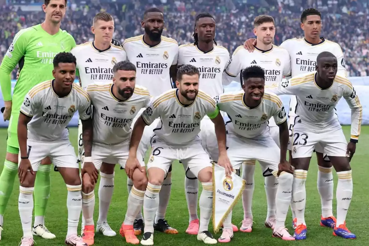 Jugadores del Real Madrid posando para una foto de equipo antes de un partido, vistiendo el uniforme blanco del club con el patrocinador "Emirates Fly Better".