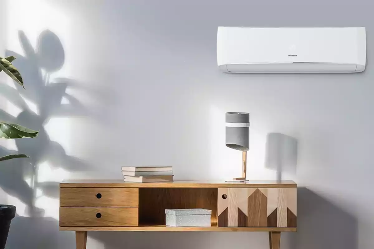 Una habitación con una pared gris claro, un aire acondicionado montado en la pared, una mesa de madera con libros, una caja y una lámpara moderna, y una planta cuyas sombras se proyectan en la pared. Una habitación con una pared gris claro, un aire acondicionado montado en la pared, una mesa de madera con libros, una caja y una lámpara moderna, y una planta cuyas sombras se proyectan en la pared.