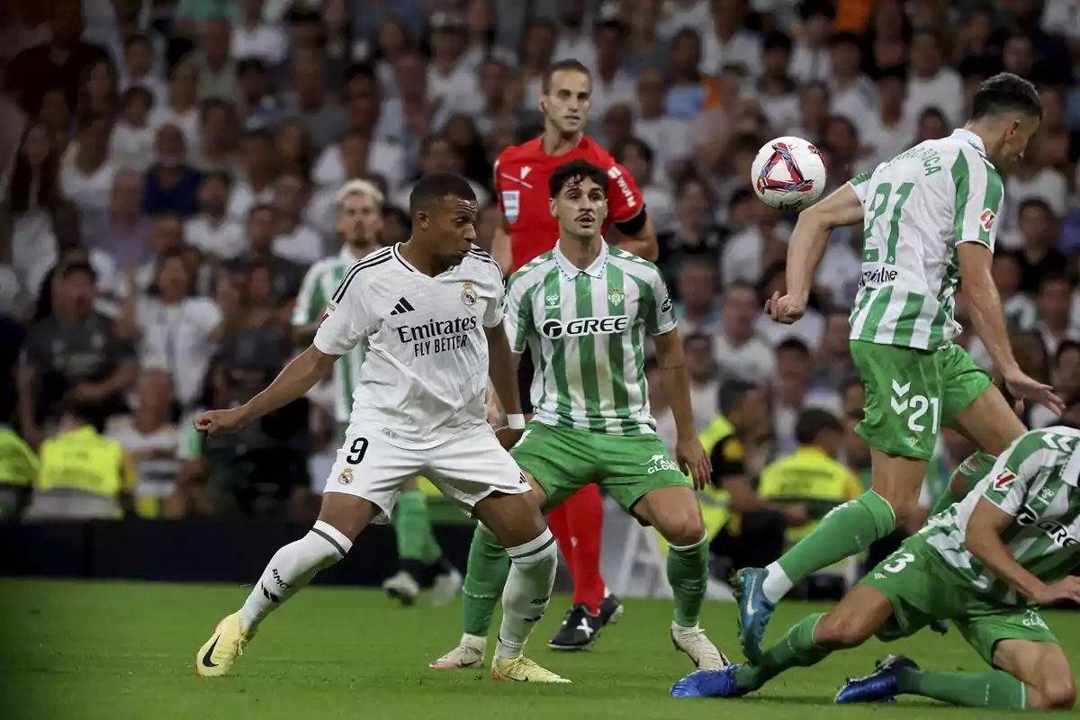 Jugadores de fútbol en acción durante un partido, uno con uniforme blanco y otros con uniforme verde y blanco, con un árbitro al fondo y público en las gradas. Jugadores de fútbol en acción durante un partido, uno con uniforme blanco y otros con uniforme verde y blanco, con un árbitro al fondo y público en las gradas.