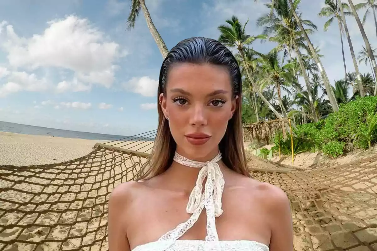 Una mujer con un vestido blanco posando frente a una playa con palmeras y una hamaca.