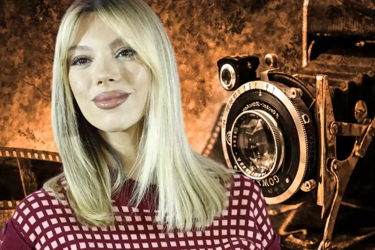 Una mujer rubia con un suéter rojo posando frente a un fondo con una cámara vintage.