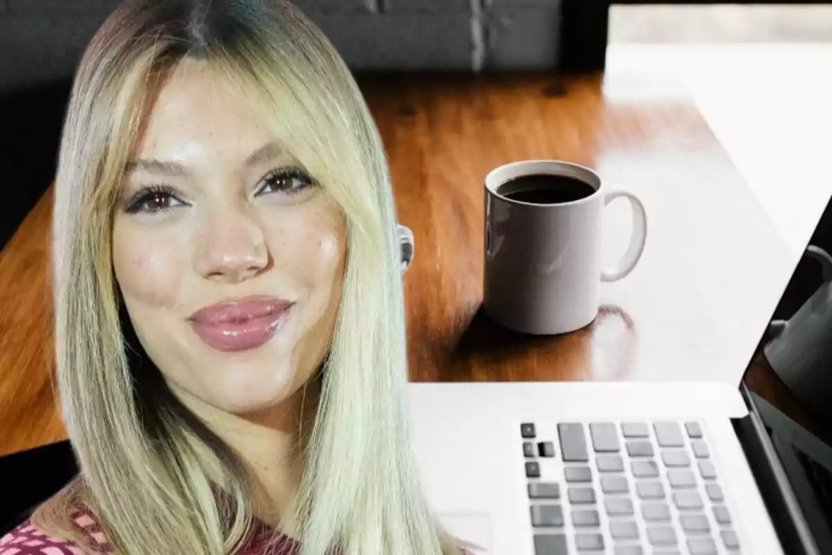 Una persona rubia sonriente frente a una mesa con una taza de café y una computadora portátil.