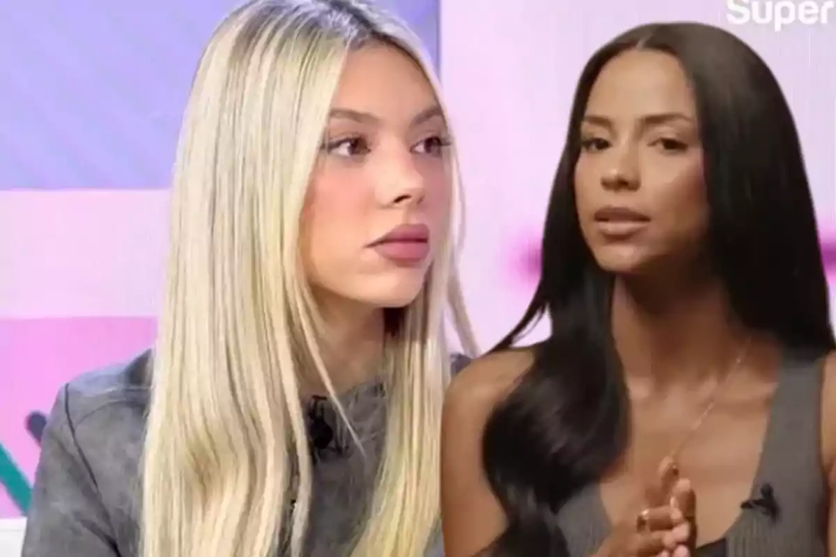 Dos mujeres sentadas en un set de televisión, una con cabello rubio y la otra con cabello oscuro, ambas mirando hacia el frente.