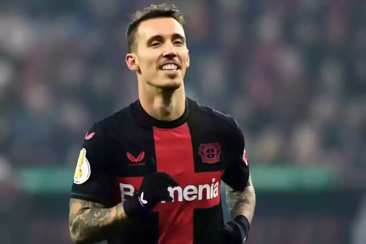 Un jugador de fútbol con uniforme negro y rojo sonríe mientras corre en el campo. Un jugador de fútbol con uniforme negro y rojo sonríe mientras corre en el campo.