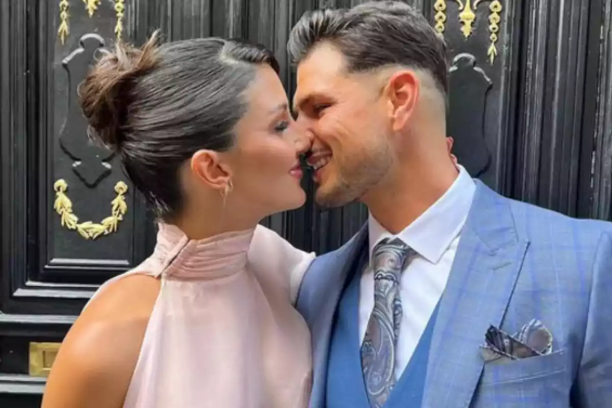 Pareja elegantemente vestida a punto de besarse frente a una puerta negra decorada con detalles dorados Pareja elegantemente vestida a punto de besarse frente a una puerta negra decorada con detalles dorados