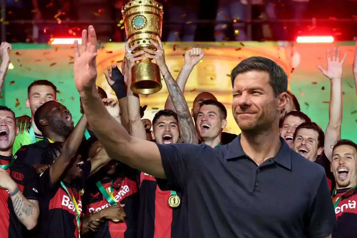 Un grupo de jugadores de fútbol celebra con un trofeo dorado mientras una persona en primer plano levanta la mano.