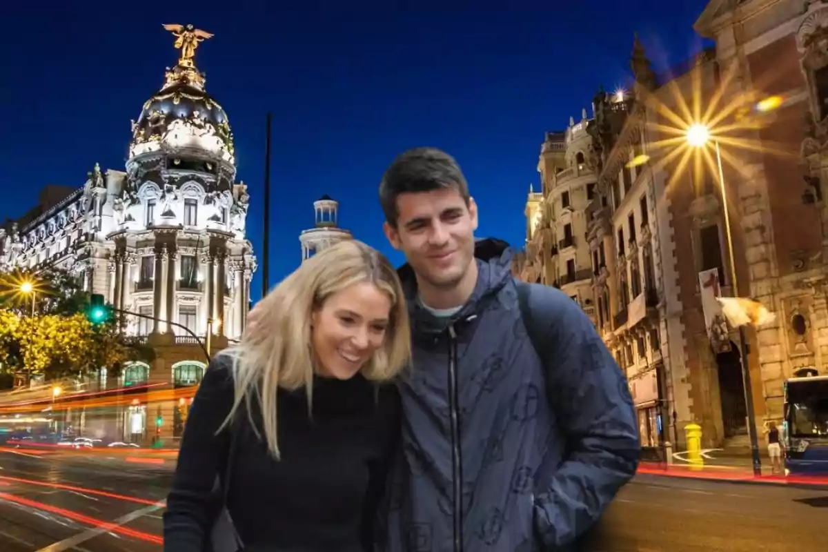 Una pareja sonriente posando frente a un edificio histórico iluminado en una ciudad por la noche.