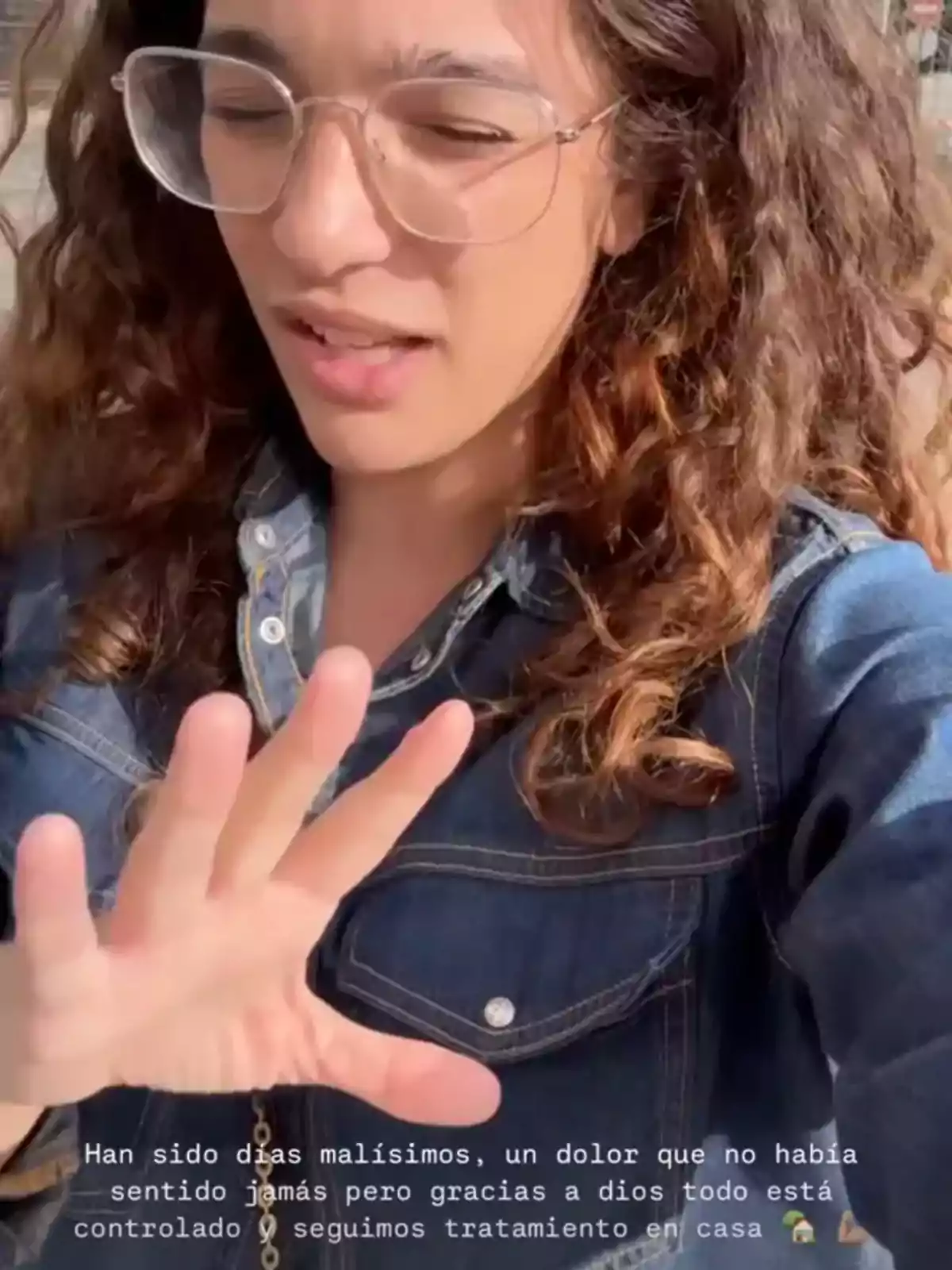 Una persona con gafas y cabello rizado está al aire libre, con los ojos cerrados y la mano levantada. Lleva una chaqueta de mezclilla y parece estar hablando o expresando algo. Una persona con gafas y cabello rizado está al aire libre, con los ojos cerrados y la mano levantada. Lleva una chaqueta de mezclilla y parece estar hablando o expresando algo.