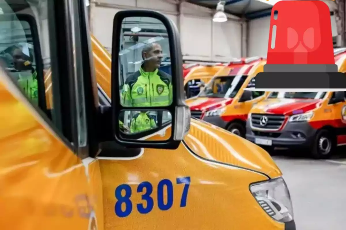 Un hombre con uniforme de emergencia se refleja en el espejo lateral de una ambulancia amarilla con el número 8307, mientras otras ambulancias están estacionadas en el fondo de un garaje.