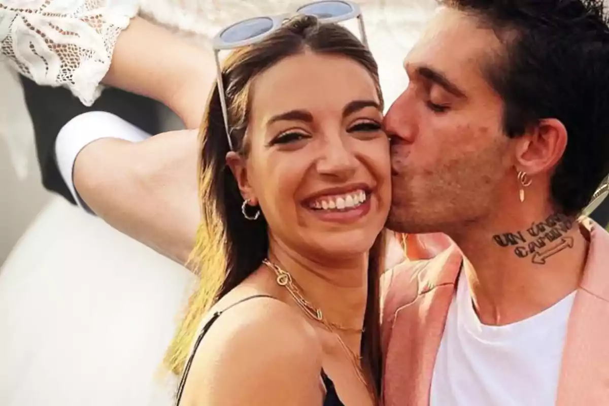 Una pareja sonriente, donde una persona besa en la mejilla a la otra, ambos lucen felices y están al aire libre.