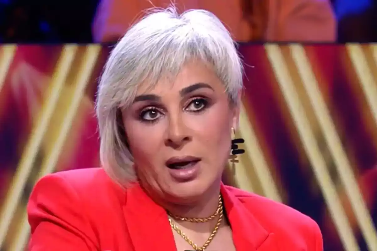 Una persona con cabello corto y canoso lleva un traje rojo y está hablando en un entorno con luces brillantes. Una persona con cabello corto y canoso lleva un traje rojo y está hablando en un entorno con luces brillantes.