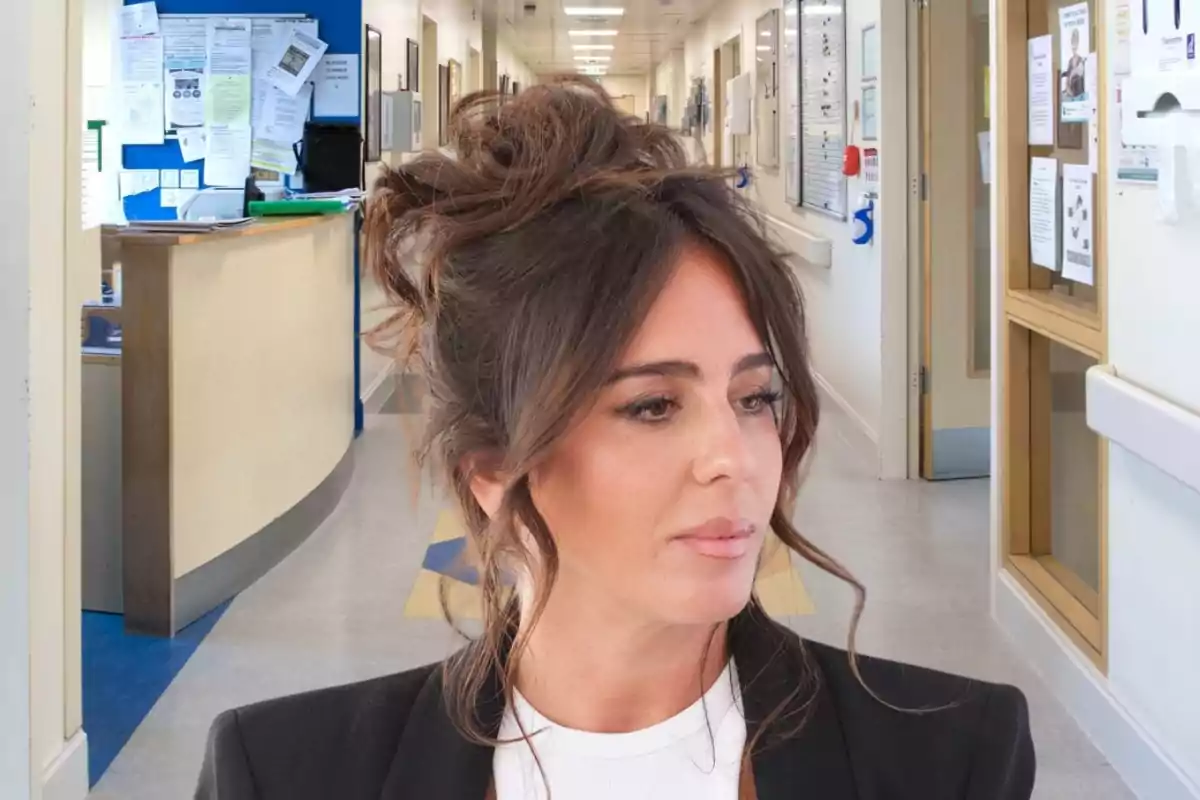 Una mujer con el cabello recogido y expresión pensativa está en un pasillo de hospital.