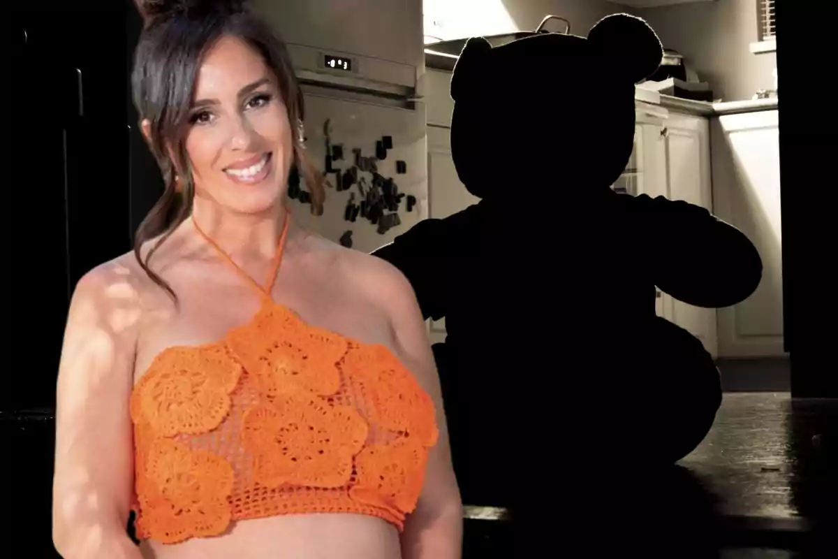 Anabel Pantoja vestida con un top naranja embarazada y un oso de peluche negro en sombras detrás