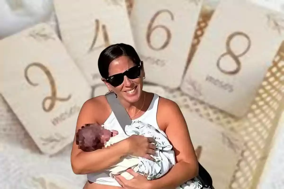 Una mujer sonriente con gafas de sol sostiene a un bebé envuelto en una manta, con un fondo de tarjetas numeradas que indican semanas o meses.