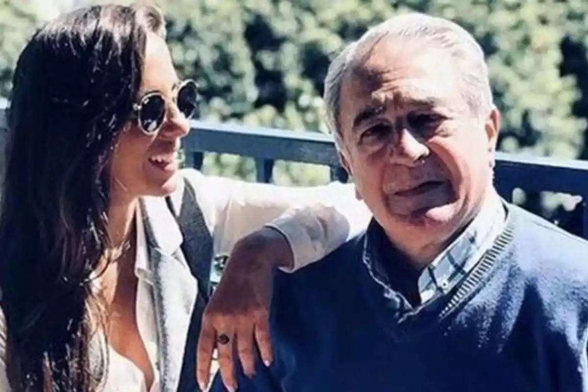 Una mujer con gafas de sol y un hombre mayor posan juntos al aire libre, con árboles desenfocados en el fondo. Una mujer con gafas de sol y un hombre mayor posan juntos al aire libre, con árboles desenfocados en el fondo.