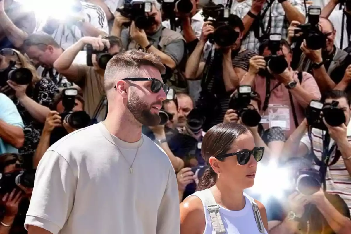 Una pareja con gafas de sol camina frente a un grupo de fotógrafos que toman fotos con cámaras profesionales.