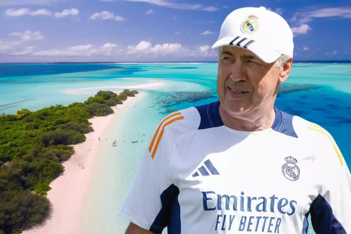 Hombre con gorra y camiseta de un equipo de fútbol posando frente a una playa de aguas cristalinas y arena blanca.