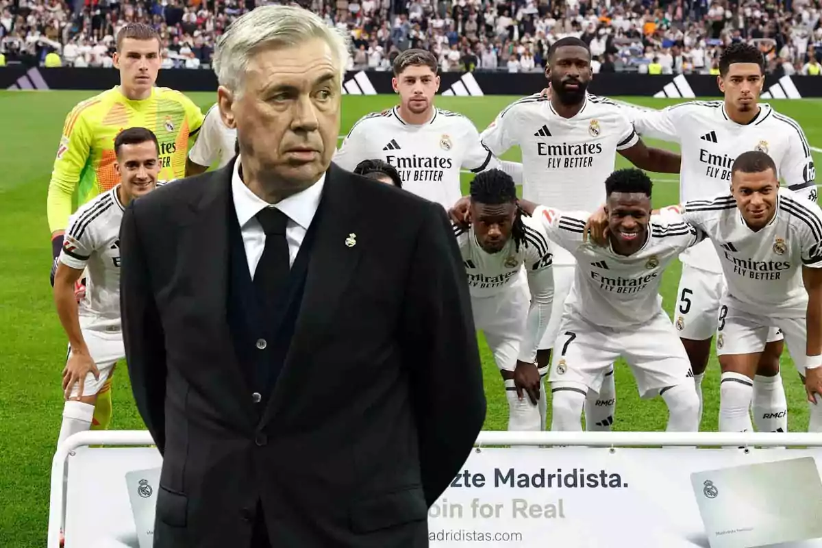 Un entrenador de fútbol en traje oscuro está de pie frente a un grupo de jugadores del Real Madrid que posan en el campo antes de un partido.