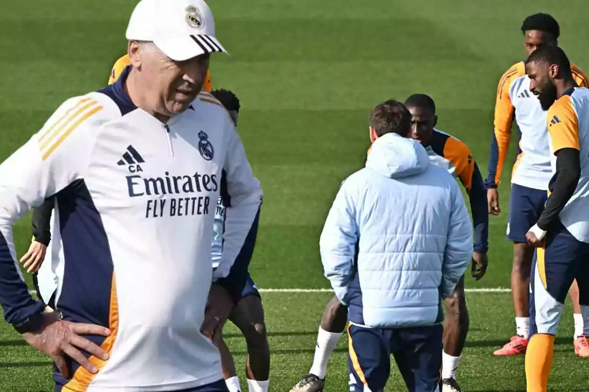 Un entrenador de fútbol con gorra blanca observa a los jugadores durante un entrenamiento en el campo.