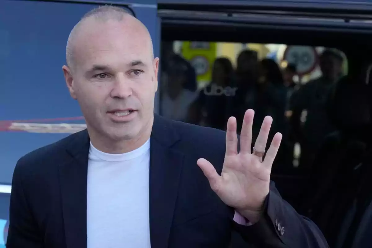 Hombre calvo con chaqueta oscura y camiseta blanca levantando la mano frente a un vehículo. Hombre calvo con chaqueta oscura y camiseta blanca levantando la mano frente a un vehículo.