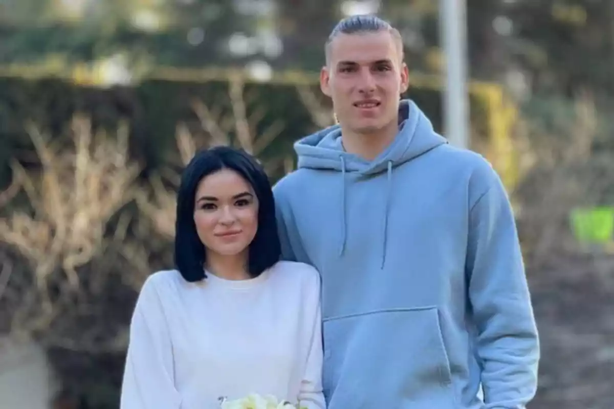 Una pareja posando al aire libre, la mujer lleva una blusa blanca y el hombre una sudadera azul claro.